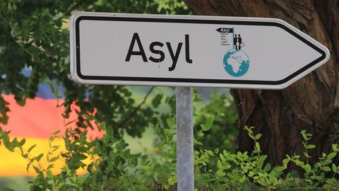 Schild mit der Aufschrift "Asyl" im Hintergrund eine Deutschland-Fahne