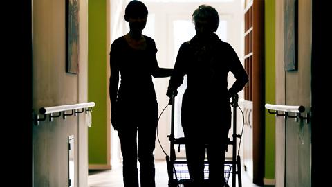 Eine Pflegekraft begleitet eine alte Frau im Pflegeheim