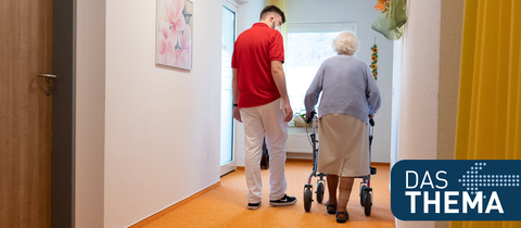 Pfleger und alte Dame mit Rollator auf dem Flur eines Altenheims