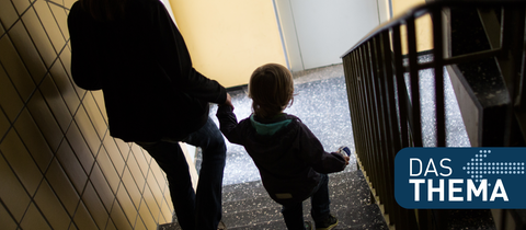 Eine Mutter geht mit ihrem kleinen Sohn durch einen Hausflur die Treppe herunter.