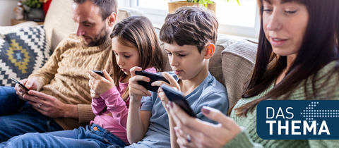 Mutter, Vater und zwei Kinder sitzen zusammen auf dem Sofa und alle schauen auf ihr Smartphone.