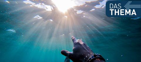 Eine Hand wird unter Wasser Richtung Wasseroberfläche gestreckt