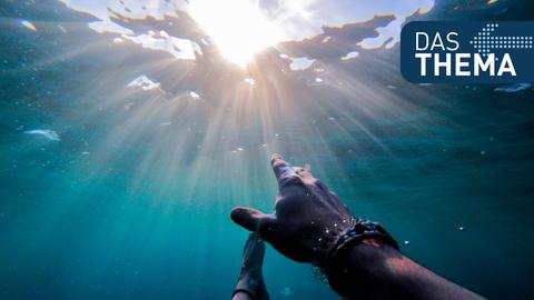 Eine Hand wird unter Wasser Richtung Wasseroberfläche gestreckt