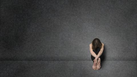 Eine Frau sitzt allein in einem dunklen Raum, den Blick nach unten gesenkt