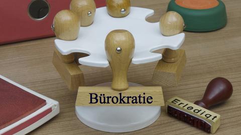 Auf einem Stempelhalter hängt ein Stempel mit der Aufschrift "Bürokratie"