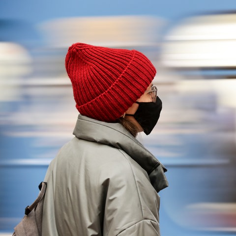 Eine Frau mit Wollmütze und Maske steht auf dem Bahngleis vor einem Zug.
