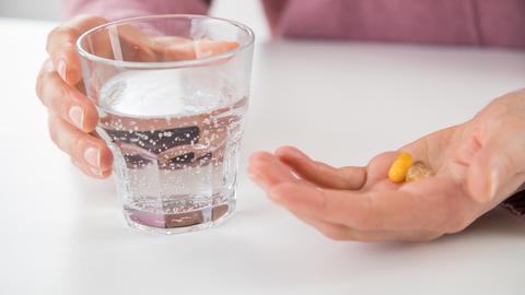 Ein Wasserglas neben einer Hand, die Medikamente zur Einnahme bereithält.