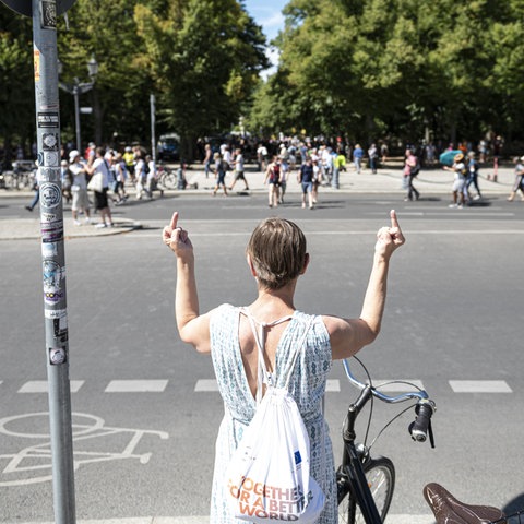 Eine Frau zeigt einem Demo-Zug gegen die Corona-Maßnahmen beide Mittelfinger.