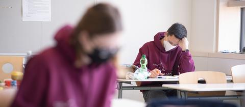 Jugendliche sitzen mit FFP2-Maske bei einer Abitur-Klausur in der Schule