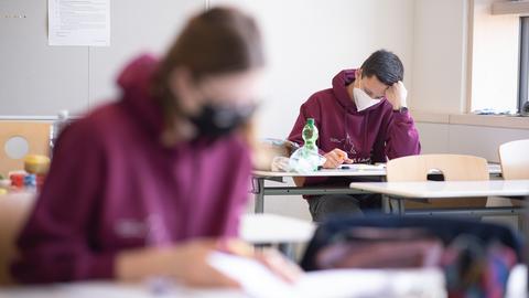 Jugendliche sitzen mit FFP2-Maske bei einer Abitur-Klausur in der Schule