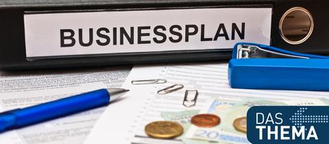Sujetbild: Ein "Businessplan"-Ordner liegt auf einem Schreibtisch neben Stift und Geld.