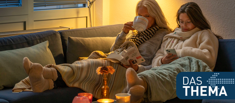 Mutter und Tochter sitzen mit Wolldecke und Tee auf der Couch