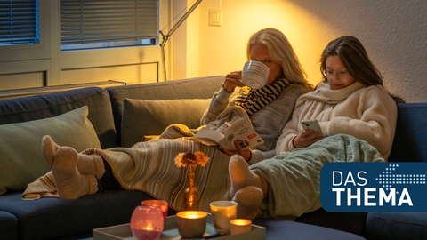 Mutter und Tochter sitzen mit Wolldecke und Tee auf der Couch