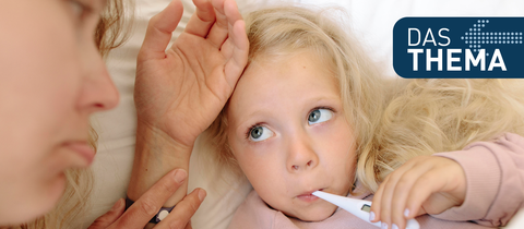 Mutter liegt neben ihrer kleinen Tochter, die ein Fieberthermometer im Mund hat