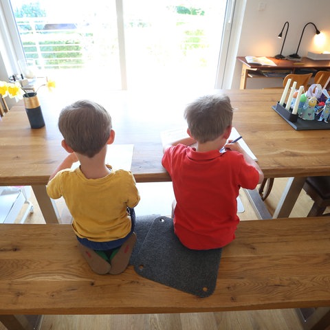 Zwei Kinder sitzen zu Hause an einem Tisch und machen Schulaufgaben.