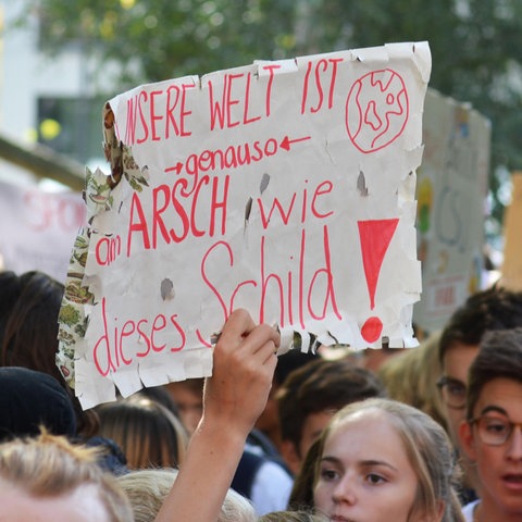 Demonstranten während des globalen Klimastreiks halten ein beschädigtes Papierschild mit der Aufschrift Unsere Welt ist so beschissen wie dieses Schild hoch
