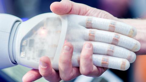 Eine Roboter-Hand und die Hand eines Menschen greifen ineinander
