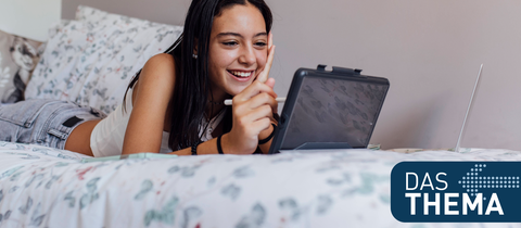 Mädchen liegt mit einem Tablet auf dem Bett