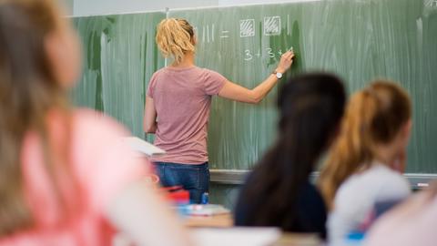 Lehrerin steht an einer Tafel in einem Klassenzimmer