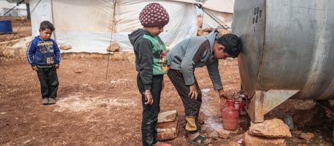 Syrische Kinder füllen Wasser aus einem Tank in eine Kanne in einem Flüchtlingslager für Binnenflüchtlinge in der Nähe des Dorfes Kafr Aruq.