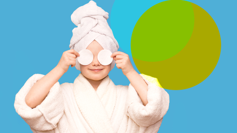 Ein Kind im Bademantel mit einem Handtuchturban auf dem Kopf, das sich zwei Wattepads vor die Augen hält und lächelt