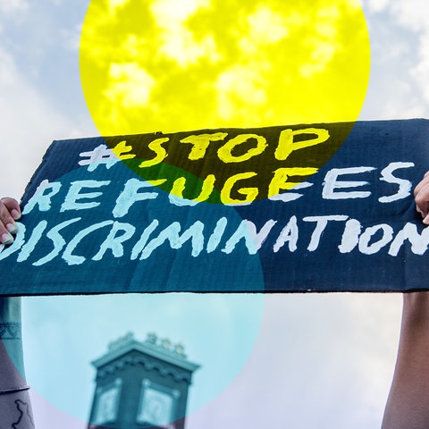 Zwei Hände halten ein Schild mit der Aufschrift "Stop Refugees Discrimination"