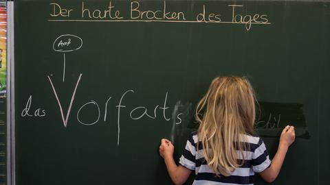 Kind steht vor einer Tafel und schreibt etwas an