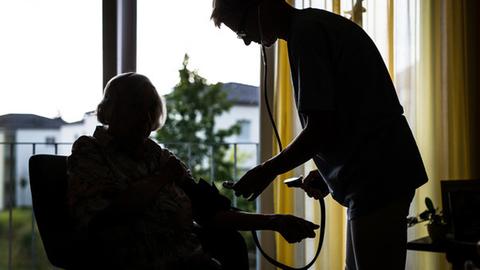 Eine Pflegerin misst in einem Heim einer älteren Dame den Blutdruck