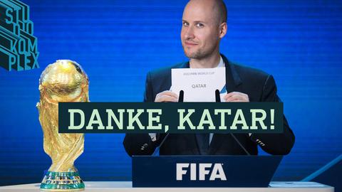 Der Host steht in dunkelblauem Sakko vor zwei Mikrofonen der FIFA und hält das gerade gezogene Los in die Kamera auf der das Land "Quatar" zu lesen ist.