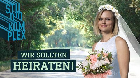 Die Hostin Anne trägt ein weißes Hochzeitskleid mit Schleier, einem Blumenkranz auf dem Kopf, hält den Brautstrauß in der Hand und schaut glücklich in die Kamera. Im Hintergrund ein sommerlicher, sonnendurchfluteter Park.
