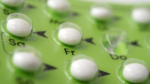 Weiße Pillen in durchsichtiger Verpackung mit grünem Grund