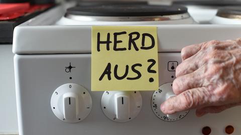 Ein Klebezettel mit dem Schriftzug "Herd aus?" klebt an einem Herd neben den Drehknöpfen.