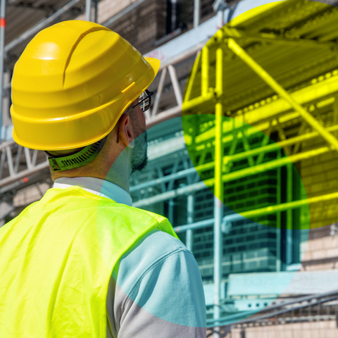 Mann mit Helm steht vor einer Baustelle