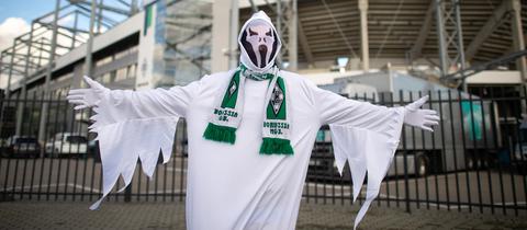 Ein Mann in einem Gespensterkostüm steht mit Gladbach-Schal um den Hals vor dem Bökelberg.