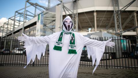 Ein Mann in einem Gespensterkostüm steht mit Gladbach-Schal um den Hals vor dem Bökelberg.