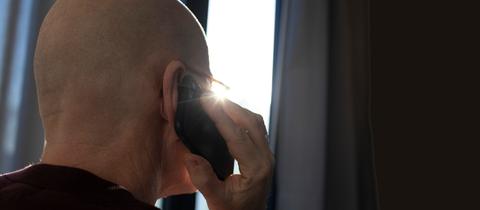 Sujetbild, Ansicht von hinten: Ein Mann mit Glatze hält sein Handy ans Ohr. 