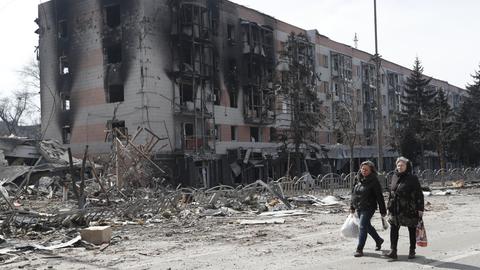 Zivilisten laufen vor zerstörten Gebäuden in Mariupol.