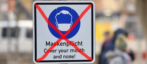 Symbolbild: Ein Warnschild, dass Masken getragen werden müssen, ist durchgestrichen