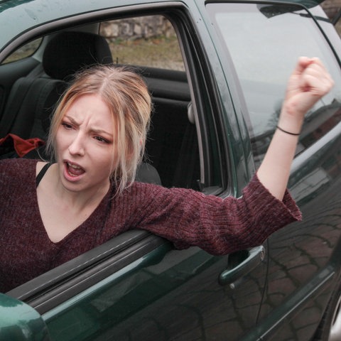 Eine junge Frau im Auto schimpft und hebt drohend die Faust