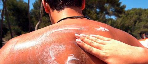 Der Rücken eines Mannes wird mit Sonnencreme eingeschmiert.