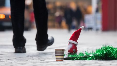 Ein kleiner Weihnachtsmann steht bei einem Pappbecher eines Obdachlosen, der auf Spenden hofft.