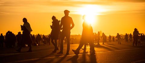 Menschen spazieren während des Sonnenuntergangs bei frühlingshaften Temperaturen auf dem Tempelhofer Feld.
