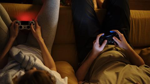 Frau und Mann sitzen auf Couch mit PlayStation Controllern in der Hand