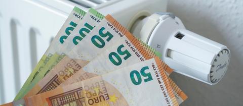 Drei 50-Euro- und zwei 100-Euro-Scheine werden vor eine ausgestellte Heizung gehalten.