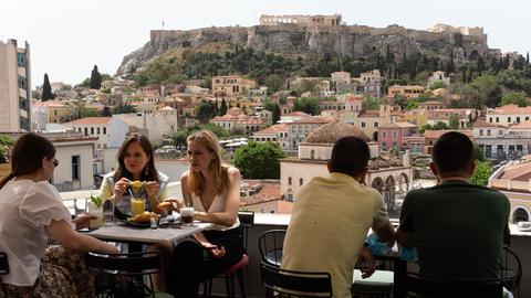 Menschen sitzen in einem Café, im Hintergrund die Akropolis