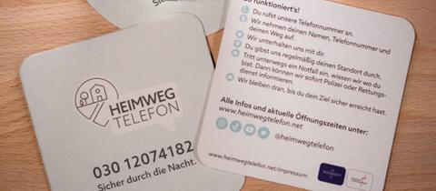 Bierdeckel mit Informationen zum Heimwegtelefon - Aufschrift: Sicher durch die Nacht und Telefonnummer 030/12074182