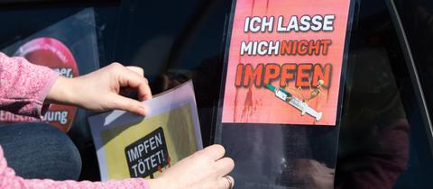 Eine Teilnehmerin eines Autokorsos klebt auf einem Parkplatz an der Autobahn 4 ein Schild mit der Aufschrift "Impfen tötet" auf die Heckscheibe eines Fahrzeugs.