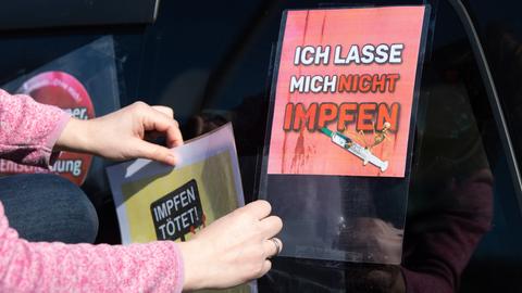 Eine Teilnehmerin eines Autokorsos klebt auf einem Parkplatz an der Autobahn 4 ein Schild mit der Aufschrift "Impfen tötet" auf die Heckscheibe eines Fahrzeugs.