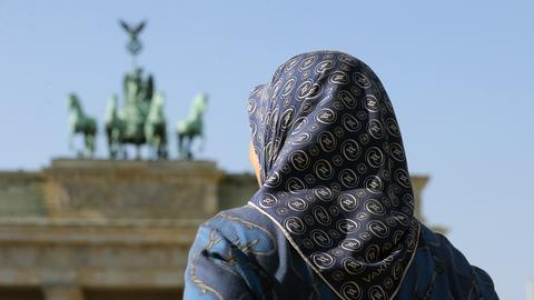 Eine Frau im Kopftuch steht vor dem Brandenburger Tor in Berlin