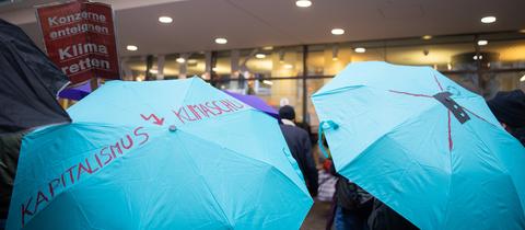 Ein Demonstrant steht mit einem Schirm, auf welchem "Kapitalismus, Klimaschutz" steht vor der Baden-Württembergischen Bank während der Demonstration am Globalen Klima Aktionstag.